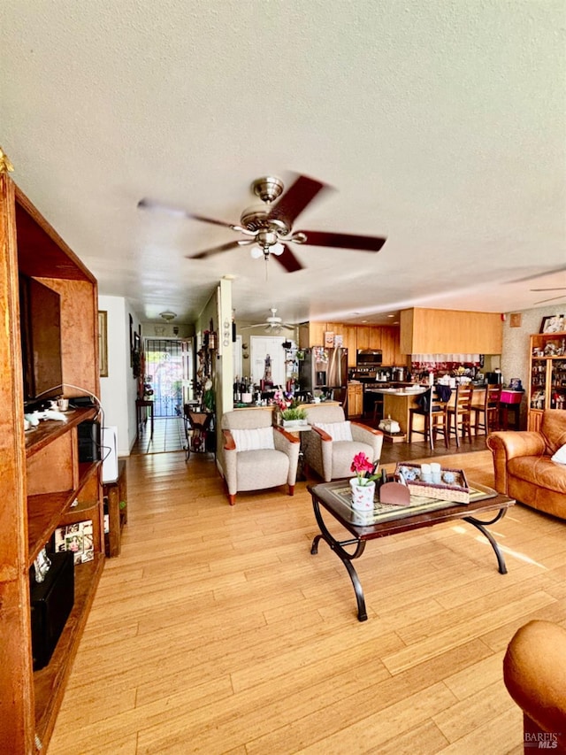living room featuring light wood-style flooring, a textured ceiling, and a ceiling fan