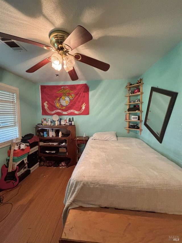 bedroom with a ceiling fan, wood finished floors, visible vents, and a textured ceiling