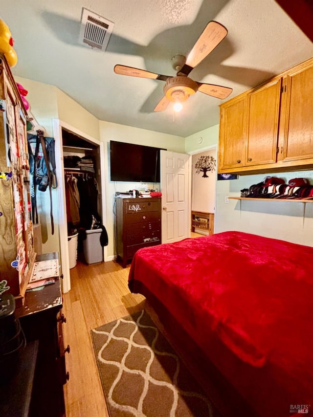 bedroom with light wood-style flooring, a textured ceiling, visible vents, a closet, and ceiling fan
