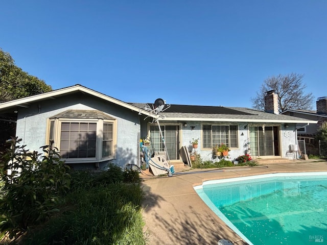rear view of property with central AC, a patio area, a chimney, an outdoor pool, and stucco siding