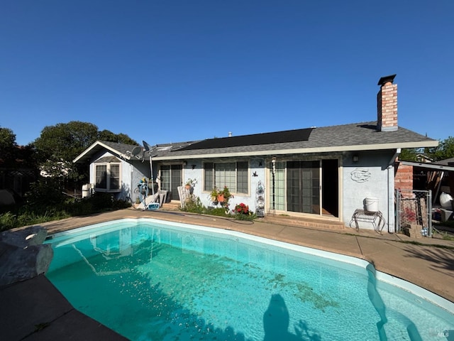 rear view of property with roof mounted solar panels, an outdoor pool, a chimney, and a patio area