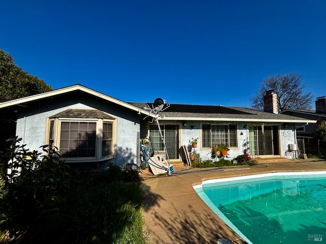 back of property with an outdoor pool, a chimney, and a patio