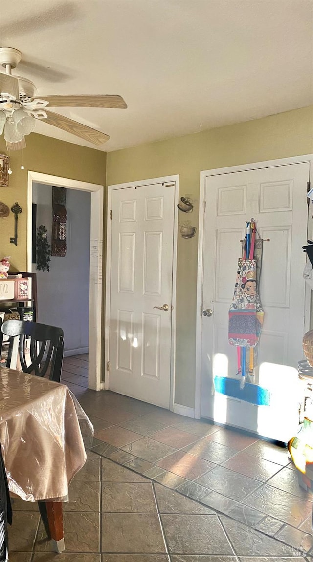 foyer entrance featuring baseboards, ceiling fan, and stone tile floors