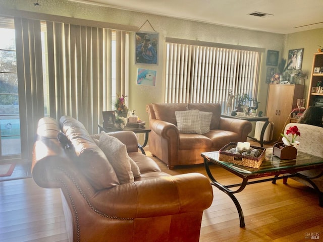 living area featuring wood-type flooring, a healthy amount of sunlight, and visible vents