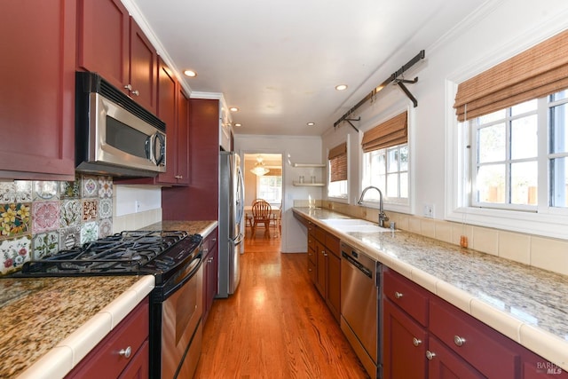 kitchen with tasteful backsplash, sink, crown molding, light hardwood / wood-style flooring, and appliances with stainless steel finishes