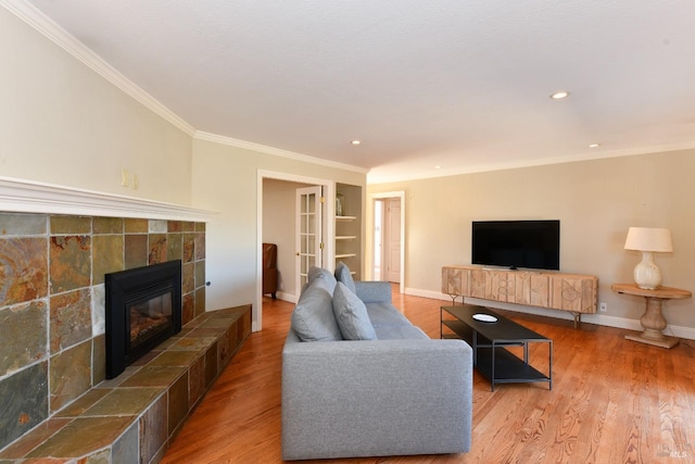 living room featuring built in shelves, wood-type flooring, a tile fireplace, and crown molding