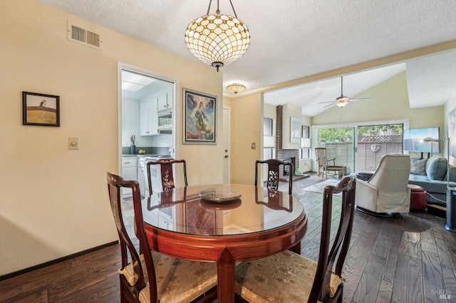 dining space with a textured ceiling, lofted ceiling, dark hardwood / wood-style flooring, a fireplace, and ceiling fan