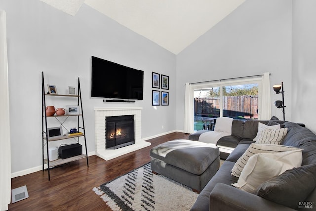 living room featuring dark wood-type flooring, a brick fireplace, and high vaulted ceiling