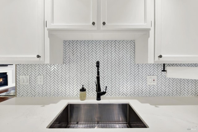 kitchen with backsplash, white cabinets, a tile fireplace, and sink