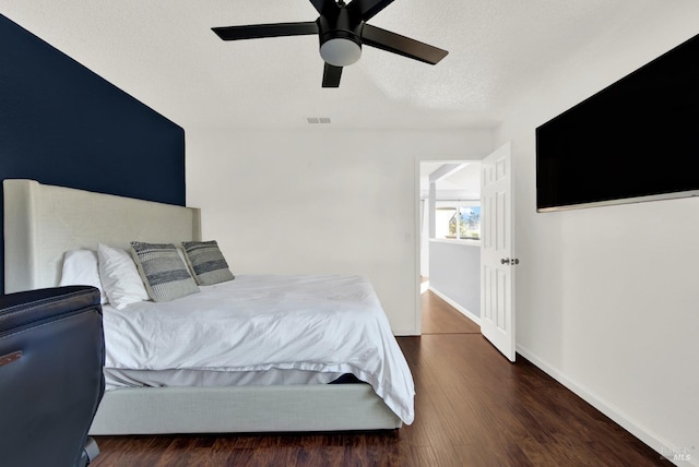 bedroom with ceiling fan, dark wood-type flooring, and a textured ceiling