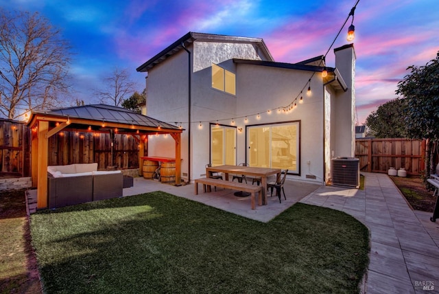 back house at dusk with a patio area, a gazebo, outdoor lounge area, central AC, and a lawn