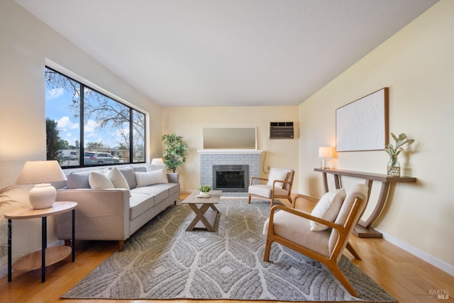 living room with a wall mounted air conditioner, a fireplace, and light wood-type flooring