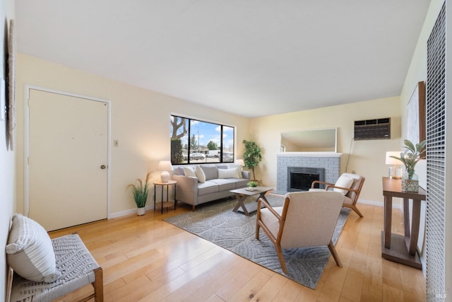 living room featuring a fireplace, light hardwood / wood-style flooring, and an AC wall unit