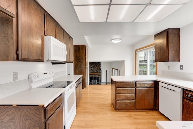 kitchen with white appliances, a stone fireplace, kitchen peninsula, and light wood-type flooring