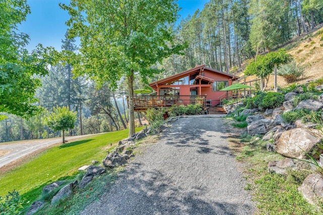 view of front facade featuring a wooden deck, gravel driveway, and a front lawn