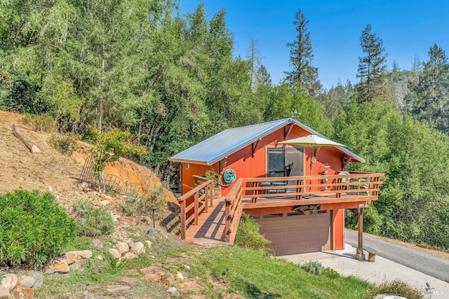 view of front of home with a deck, aphalt driveway, a wooded view, an attached garage, and metal roof