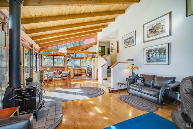 living area with stairs, lofted ceiling with beams, wooden ceiling, and a wood stove