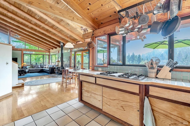 kitchen with light tile patterned flooring, stainless steel gas stovetop, vaulted ceiling with beams, tile counters, and wood ceiling