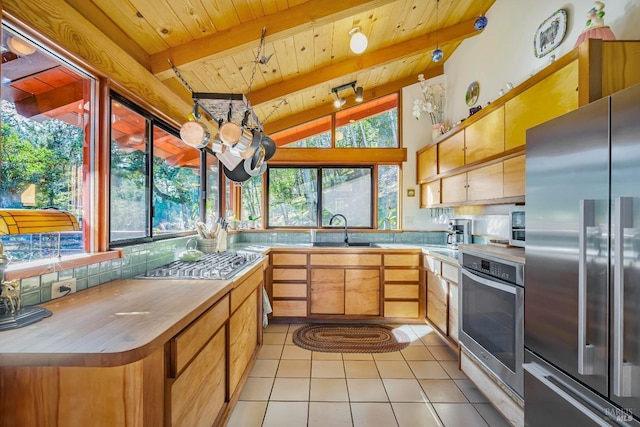 kitchen with sink, vaulted ceiling with beams, wooden ceiling, light tile patterned floors, and appliances with stainless steel finishes