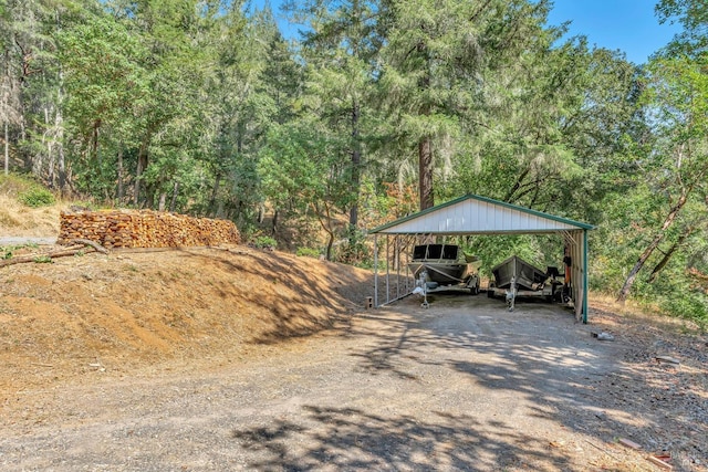 view of car parking with a detached carport, a wooded view, and driveway