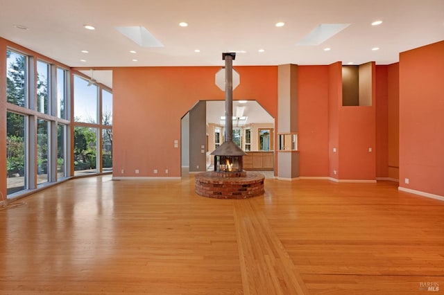 unfurnished living room featuring a skylight, floor to ceiling windows, a wood stove, a high ceiling, and light wood-type flooring