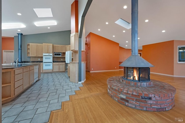 kitchen with white appliances, a skylight, a wood stove, high vaulted ceiling, and light brown cabinetry