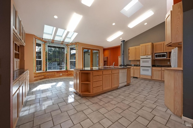 kitchen with lofted ceiling with skylight, light brown cabinetry, a center island with sink, and white appliances