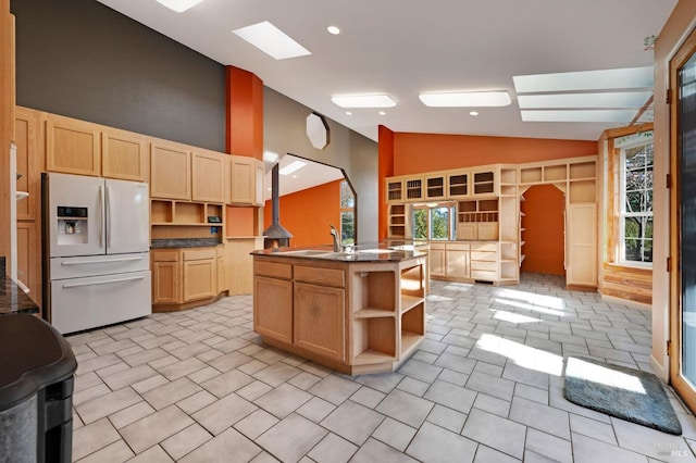 kitchen featuring vaulted ceiling, light tile patterned flooring, a kitchen island with sink, light brown cabinets, and white fridge with ice dispenser