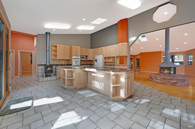 kitchen with kitchen peninsula, a wood stove, light brown cabinetry, fridge with ice dispenser, and high vaulted ceiling