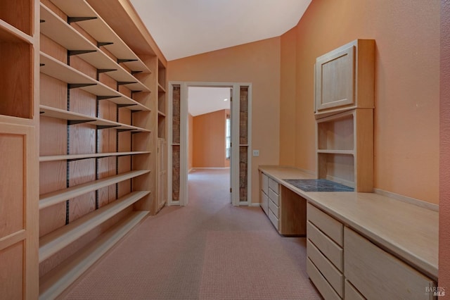 interior space featuring lofted ceiling, light brown cabinetry, built in desk, and light carpet