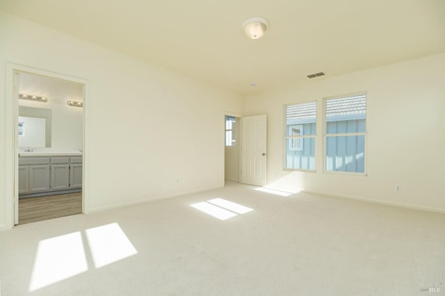 unfurnished bedroom featuring light colored carpet and ensuite bath