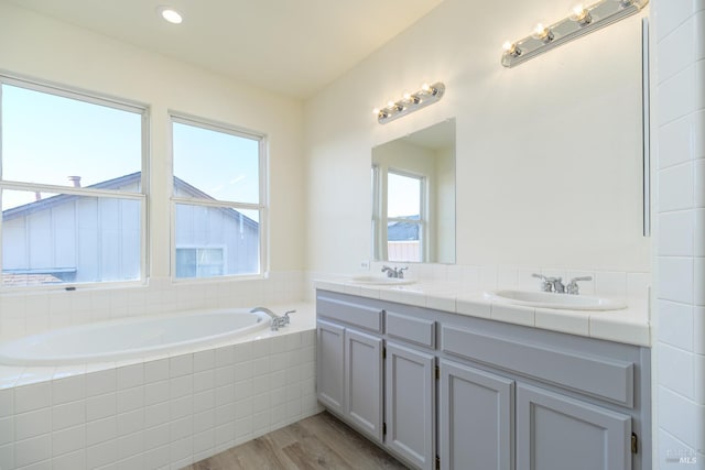 bathroom with hardwood / wood-style flooring, tiled bath, and vanity