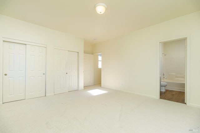 unfurnished bedroom with two closets, connected bathroom, and carpet flooring