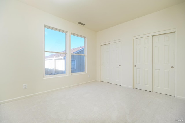 unfurnished bedroom with light colored carpet and multiple closets