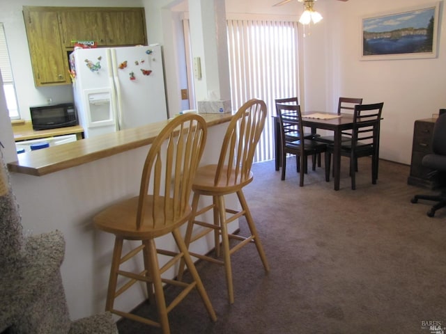 kitchen featuring a kitchen breakfast bar, white refrigerator with ice dispenser, kitchen peninsula, and dark colored carpet