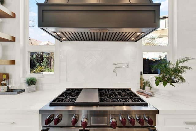 kitchen with white cabinetry, island exhaust hood, backsplash, a wealth of natural light, and stainless steel stove