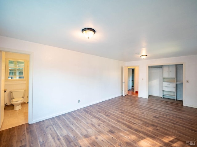 unfurnished bedroom with ensuite bathroom, a closet, and dark hardwood / wood-style flooring