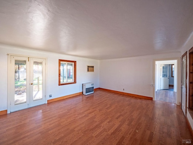 unfurnished living room featuring wood-type flooring, heating unit, and french doors