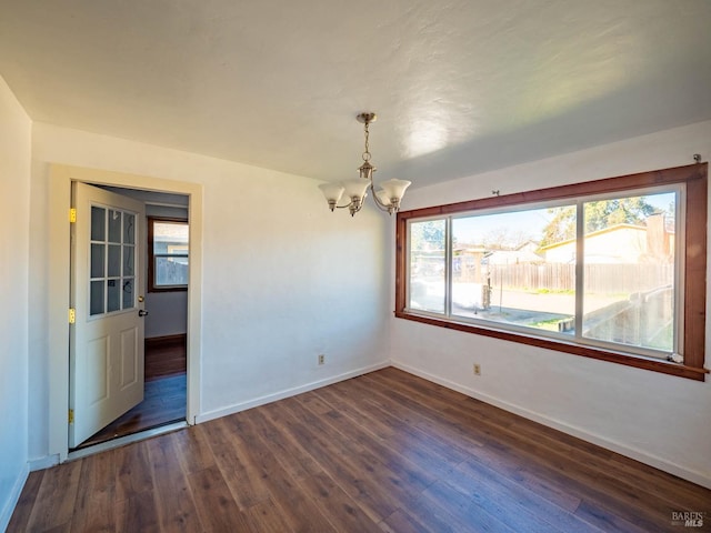 empty room with dark hardwood / wood-style flooring and an inviting chandelier