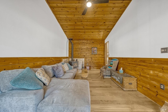 living room with lofted ceiling, wooden walls, light hardwood / wood-style flooring, wood ceiling, and a wood stove