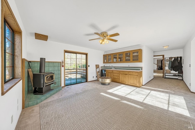 interior space with ceiling fan, a wood stove, light colored carpet, and sink