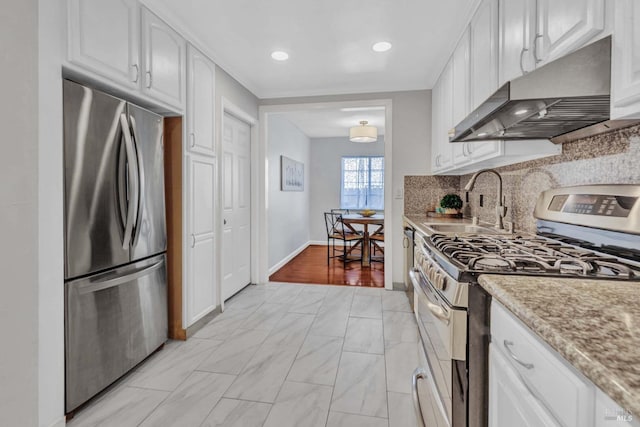 kitchen with light stone countertops, appliances with stainless steel finishes, white cabinetry, sink, and backsplash