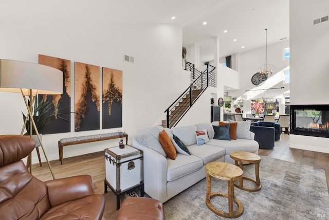 living room featuring a high ceiling, a multi sided fireplace, a chandelier, and light hardwood / wood-style floors