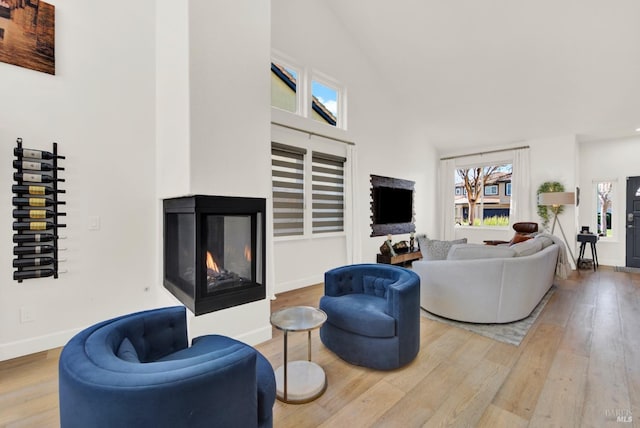 living room with hardwood / wood-style flooring, a multi sided fireplace, and high vaulted ceiling