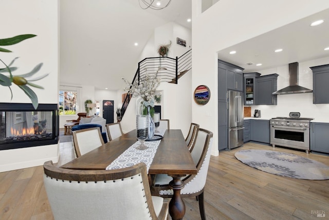 dining area featuring a high ceiling, a multi sided fireplace, and light hardwood / wood-style floors