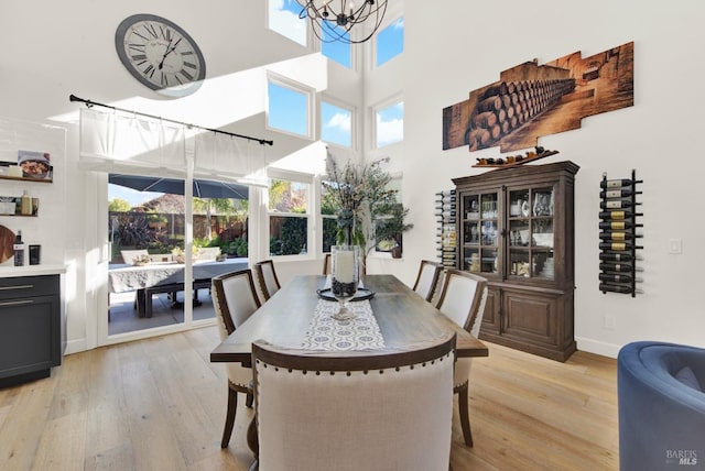 dining area featuring a notable chandelier, light hardwood / wood-style flooring, and a high ceiling