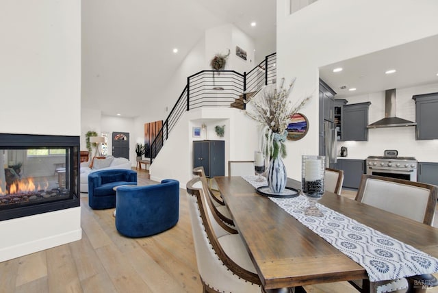 dining space with a towering ceiling, a multi sided fireplace, and light hardwood / wood-style flooring