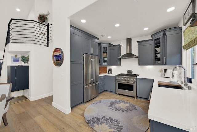 kitchen featuring sink, gray cabinets, high quality appliances, wall chimney exhaust hood, and light wood-type flooring