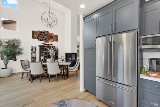 kitchen featuring gray cabinets, appliances with stainless steel finishes, hanging light fixtures, a notable chandelier, and light wood-type flooring