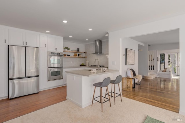 kitchen featuring a breakfast bar, decorative backsplash, appliances with stainless steel finishes, white cabinets, and wall chimney exhaust hood